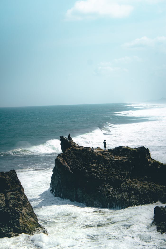 A scenic view of a person standing on a rocky cliff by the ocean, perfect for travel inspiration.